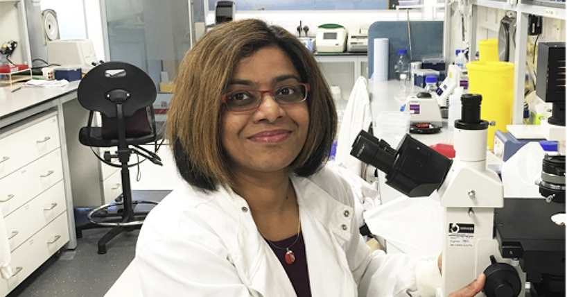 Dr Amarnath in white lab coat at microscope in laboratory